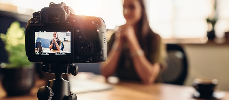 Digital camera on flexible tripod recording a video of woman at desk.